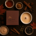 A styled flat-lay of a brown rectangular candle box labeled 'MAPLE CREAM & CHAI' surrounded by autumn spices and ingredients including cinnamon sticks, star anise, dried leaves, and two bowls containing creamy beige and amber liquid on a dark textured surface.